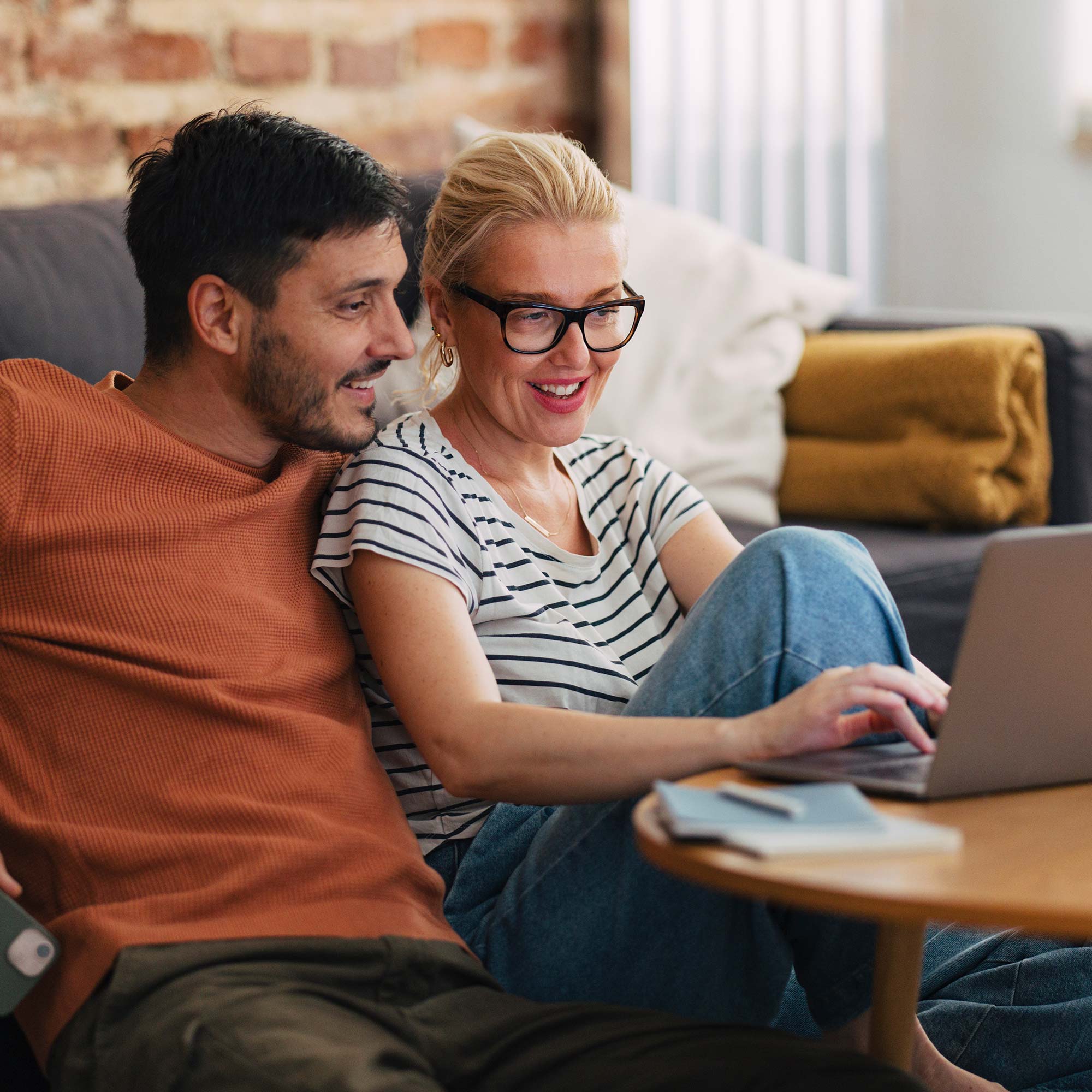 a man and woman sitting on a couch looking at a laptop