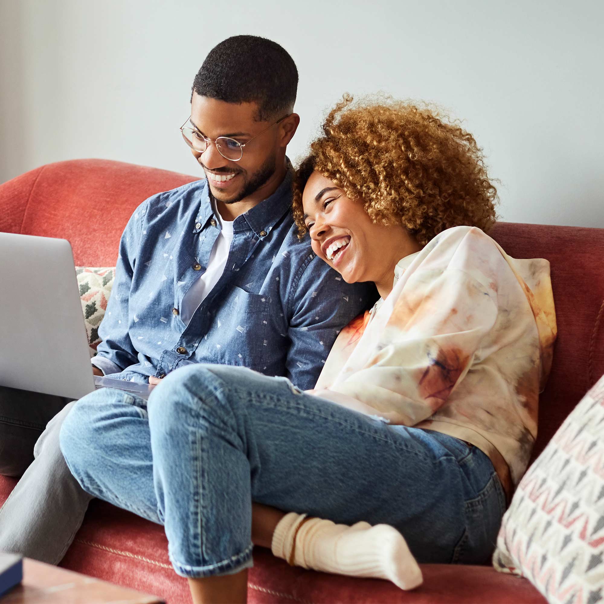 a man and woman sitting on a couch looking at a laptop