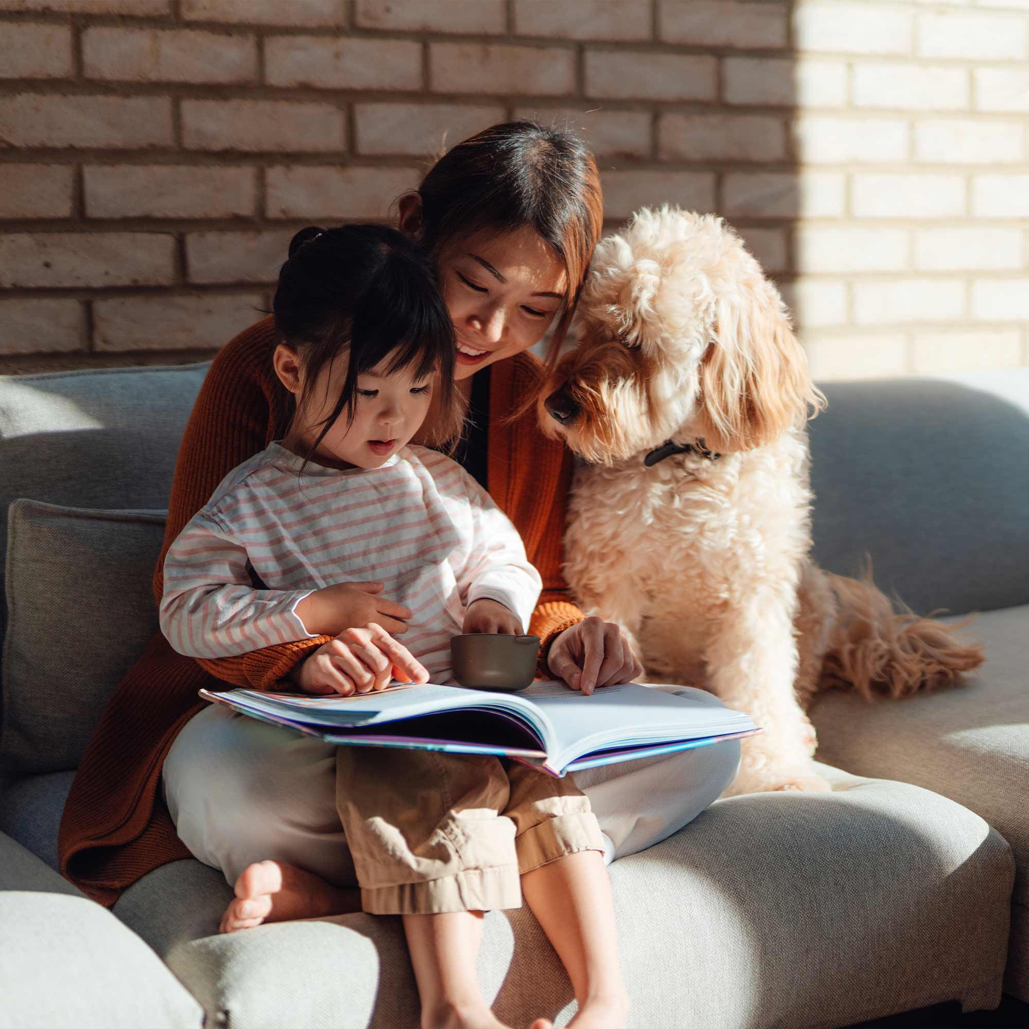 a woman and child sitting on a couch reading a book with a dog