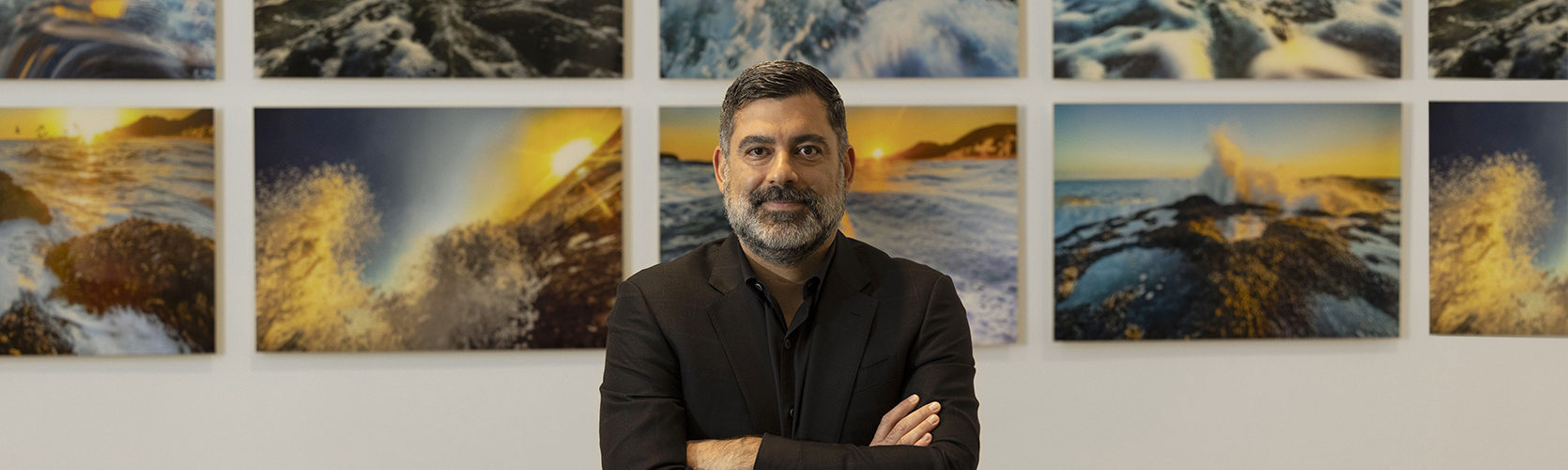 a man with his arms crossed in front of a wall of paintings