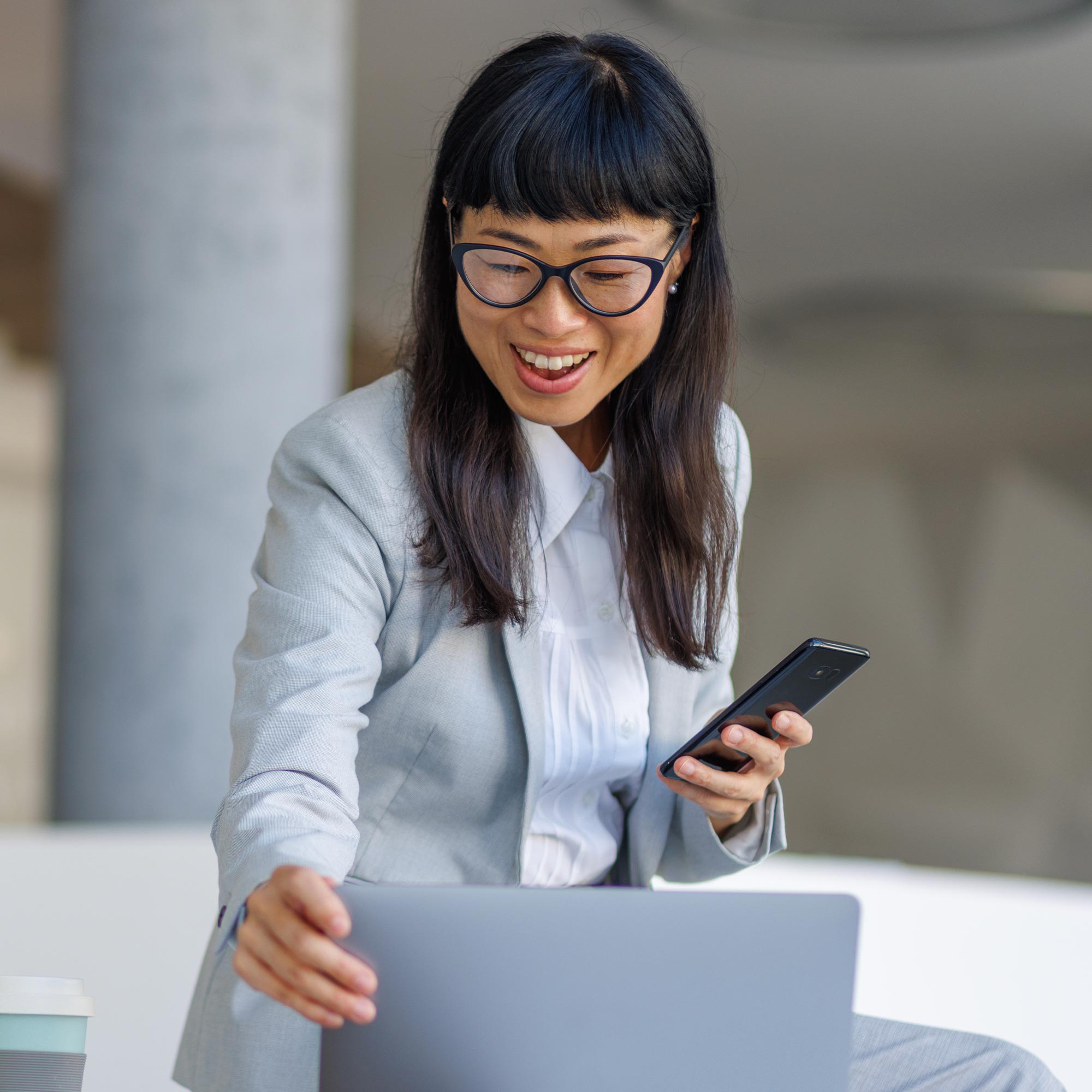 a woman in a suit holding a phone and looking at a laptop