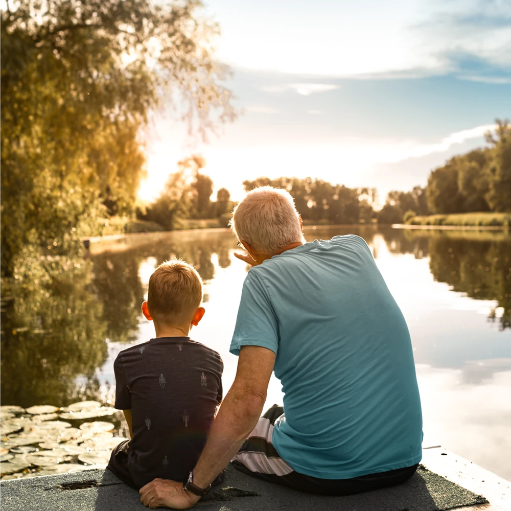 grandfather and son sitting next to a lake grandfather and son sitting next to a lake