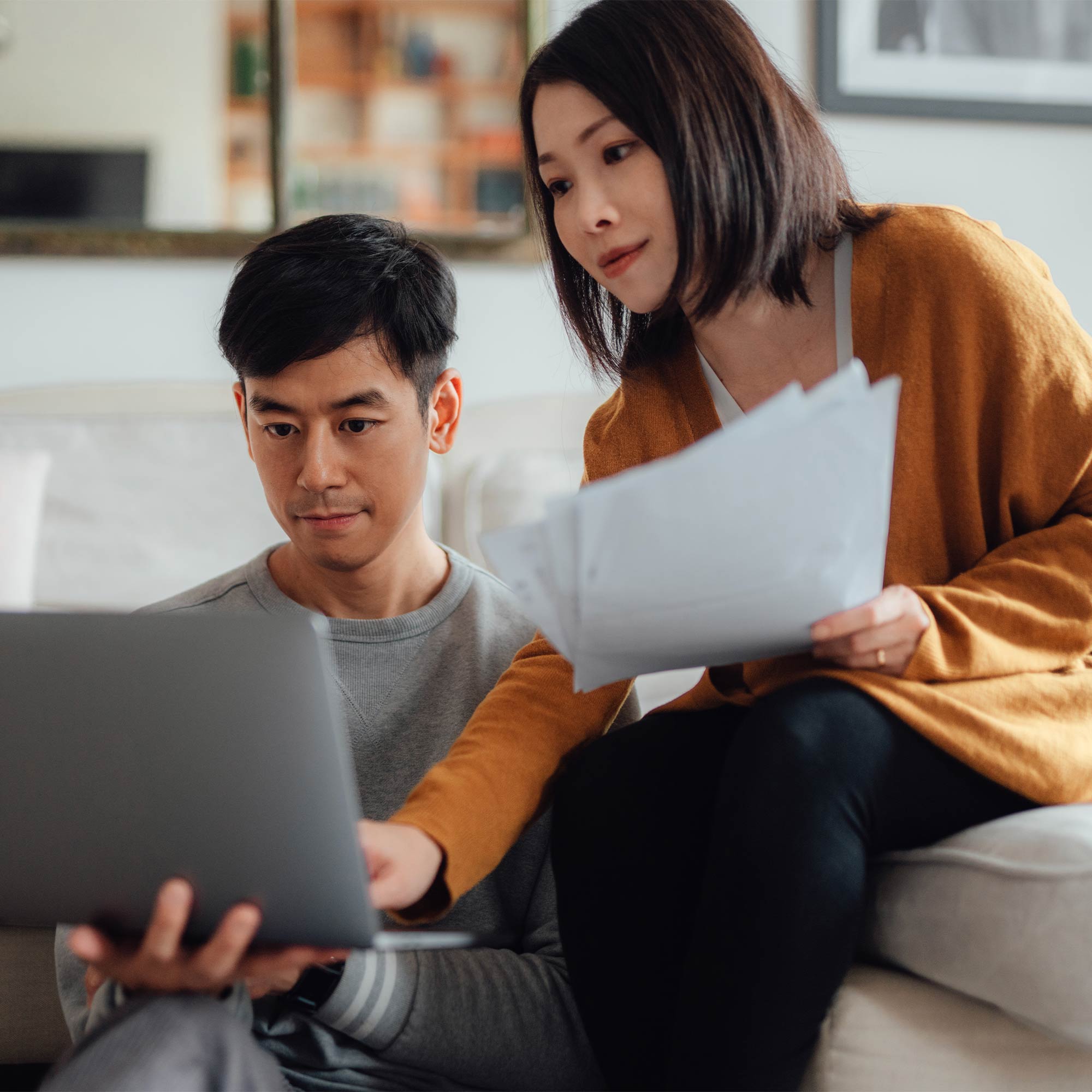a man and woman sitting on a couch looking at a laptop