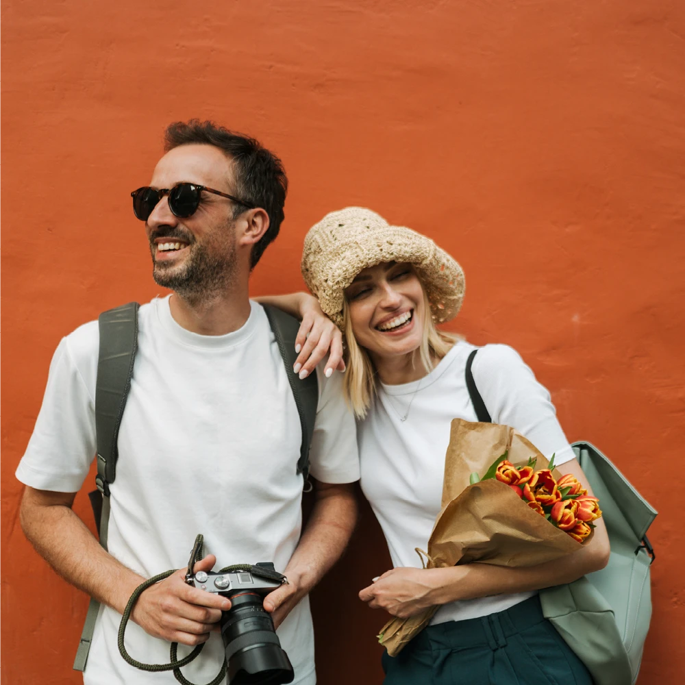 man and woman standing next to a building holding a camera and flowers man and woman standing next to a building holding a camera and flowers