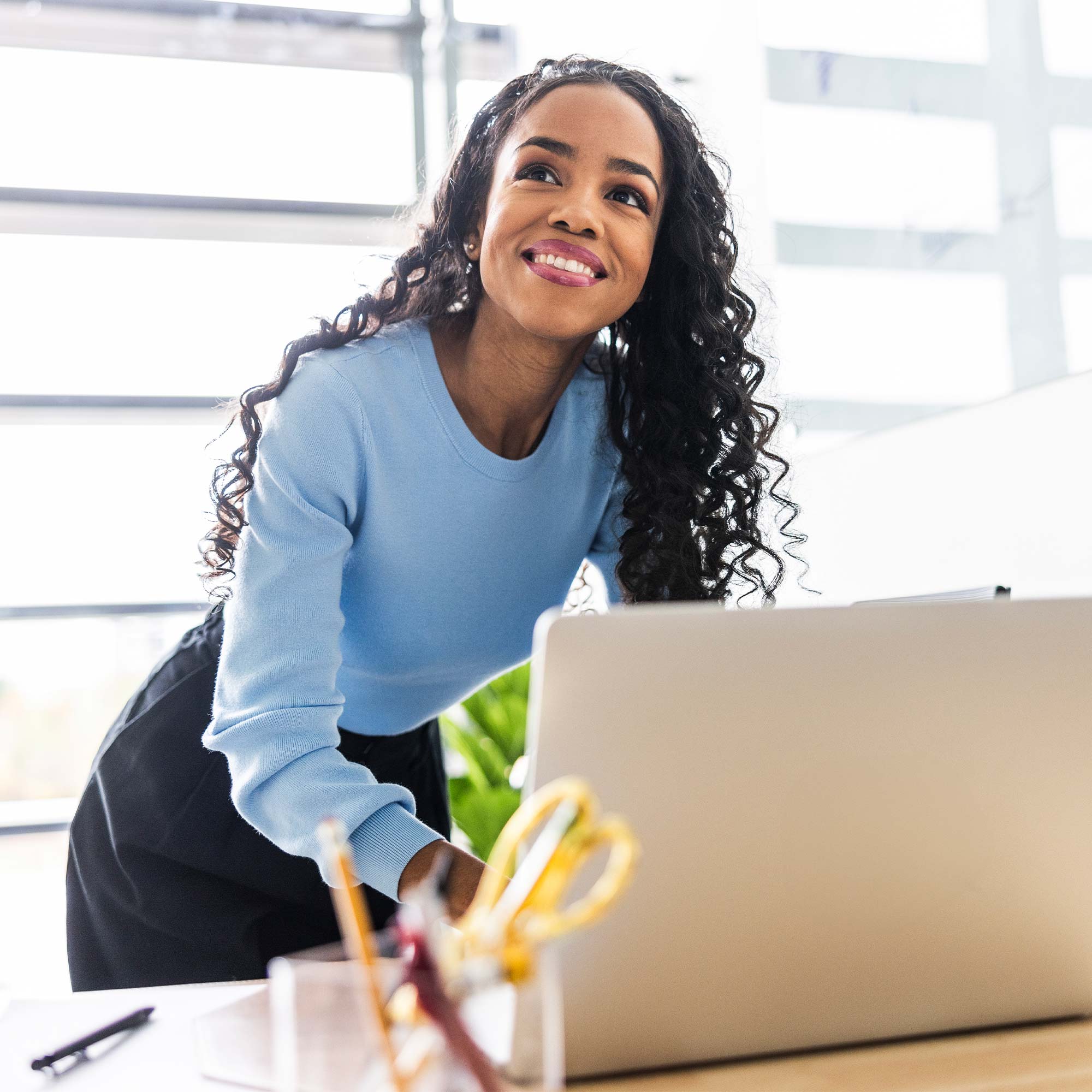 a woman leaning on a desk with a laptop