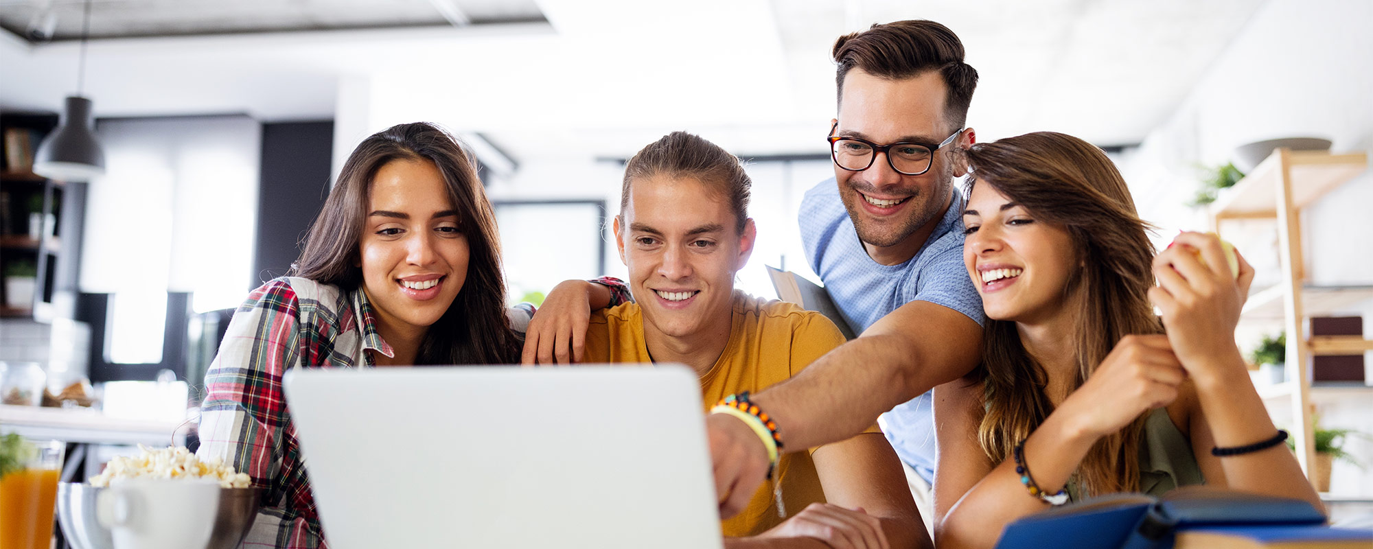 Four students are smile and laugh around a computer in the school library.