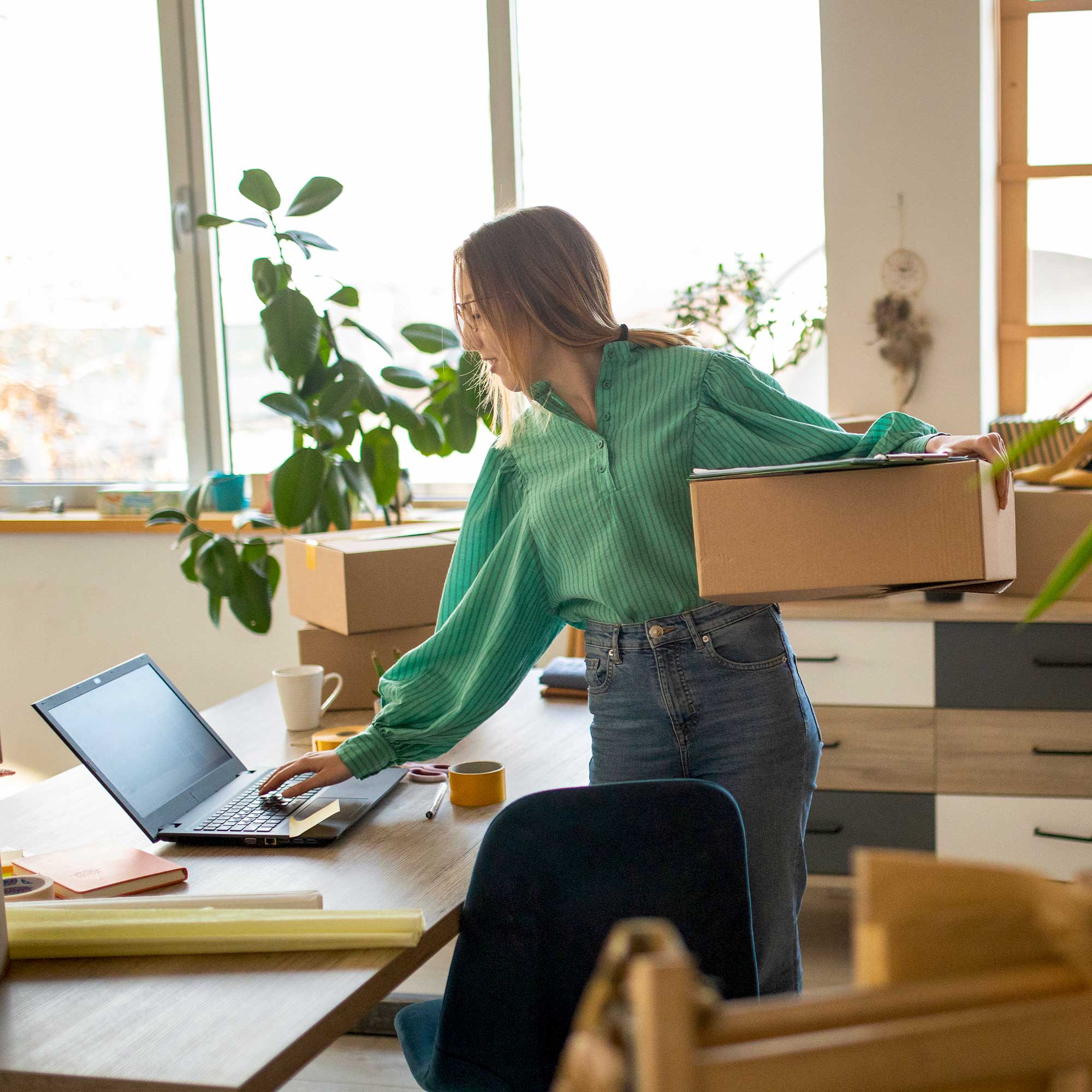 a woman holding a box and using a laptop