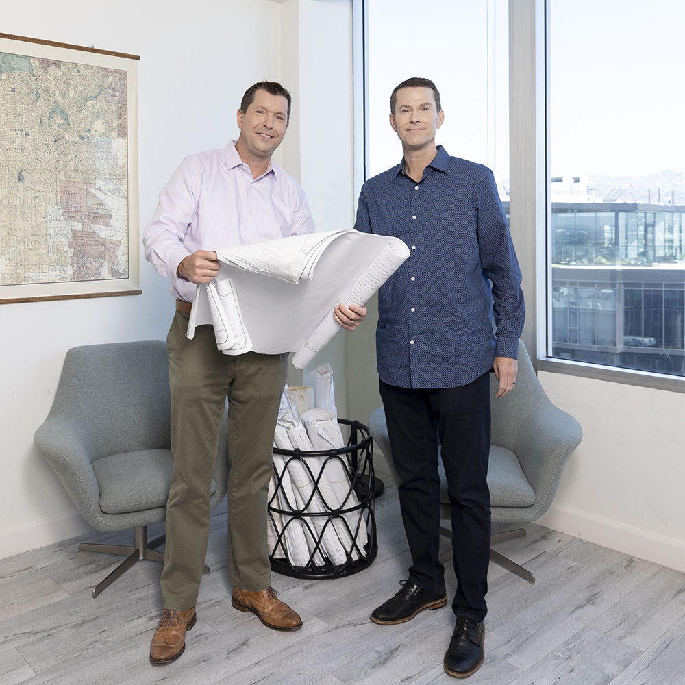 two men standing in a room holding a blueprint