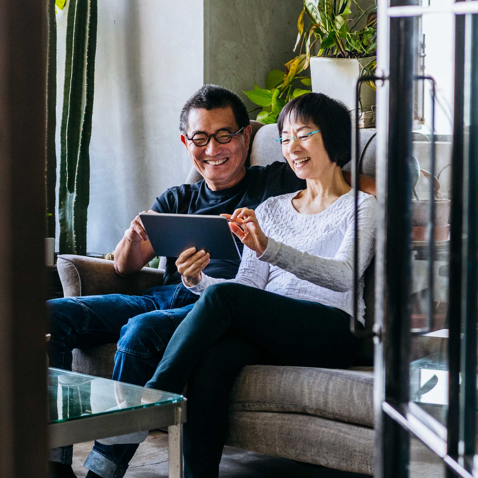 a man and woman sitting on a couch looking at a tablet