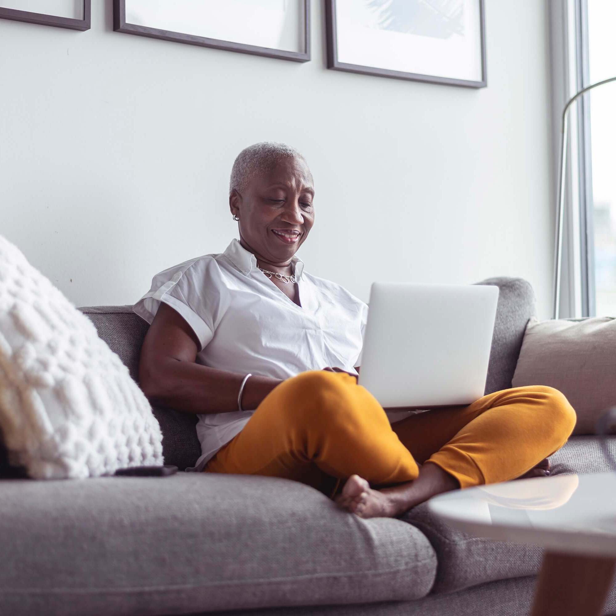 Woman wearing white shirt and orange pants sitting on a couch and using a laptop