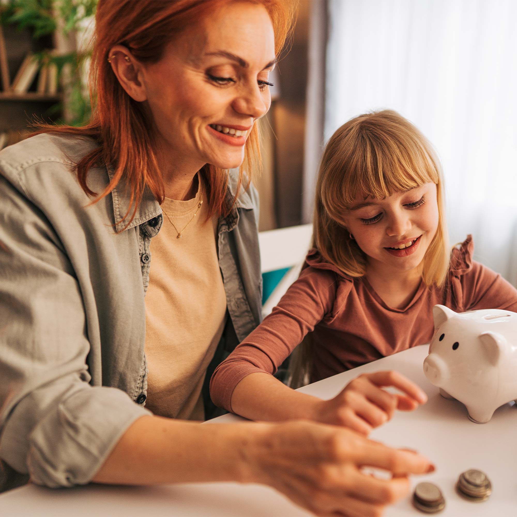 a woman and a girl sitting at a table with a piggy bank